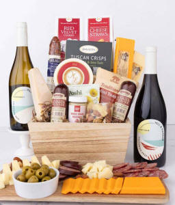 Wooden basket filled with 4 cheeses, 3 sausages, crackers, cookies, nuts, mustard, olives and crisps alongside 2 bottles of wine - Pinot Noir &amp; Chardonnay.
